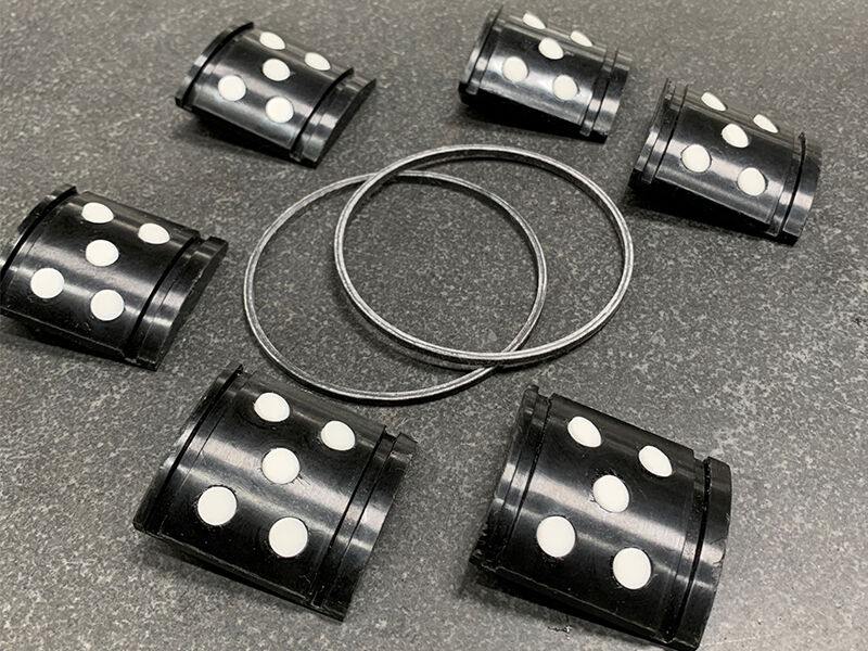 Image of several frac plug composite lower slip components laid out on a granite surface. There are six semi-circular black segments and two loops.  